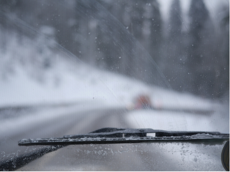 A blurry image taken from inside a car shows a snowy road and dangerous conditions due to condensation inside car windows. 