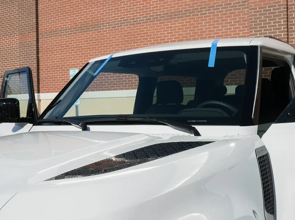 Freshly installed windshield with blue tape after replacement on a white SUV